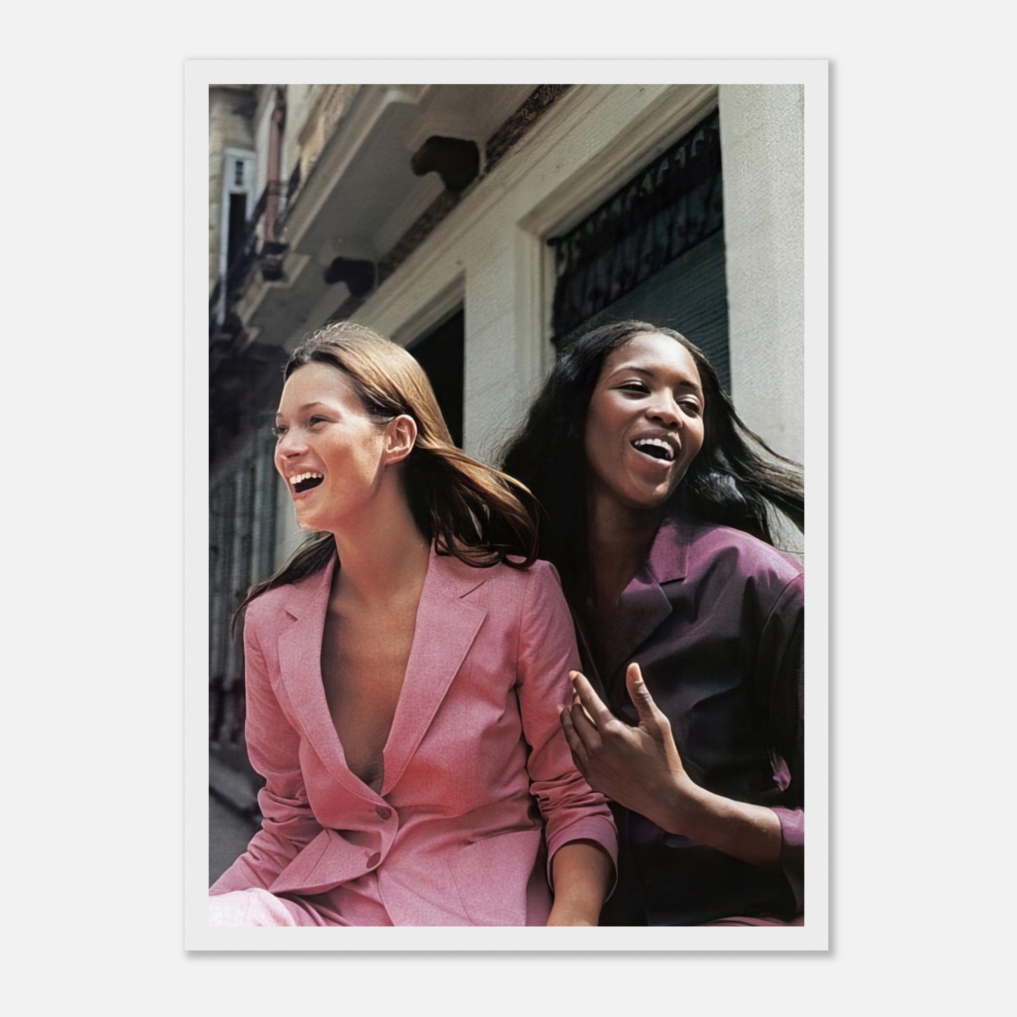 Naomi Campbell and Kate Moss laughing together in stylish suits, captured in a joyful, candid moment.