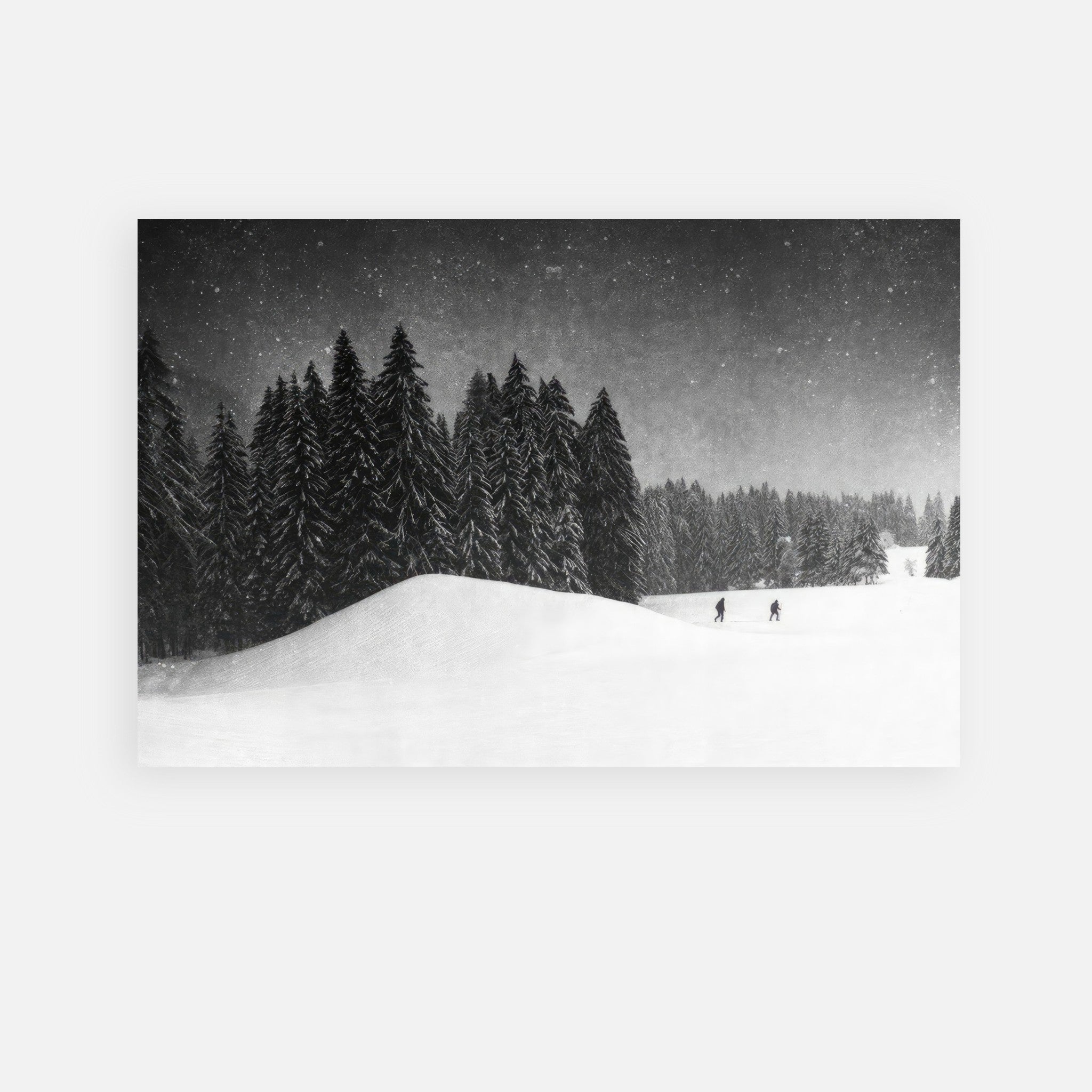 Black-and-white metal print of two figures crossing a snowy field with evergreen trees in the background.