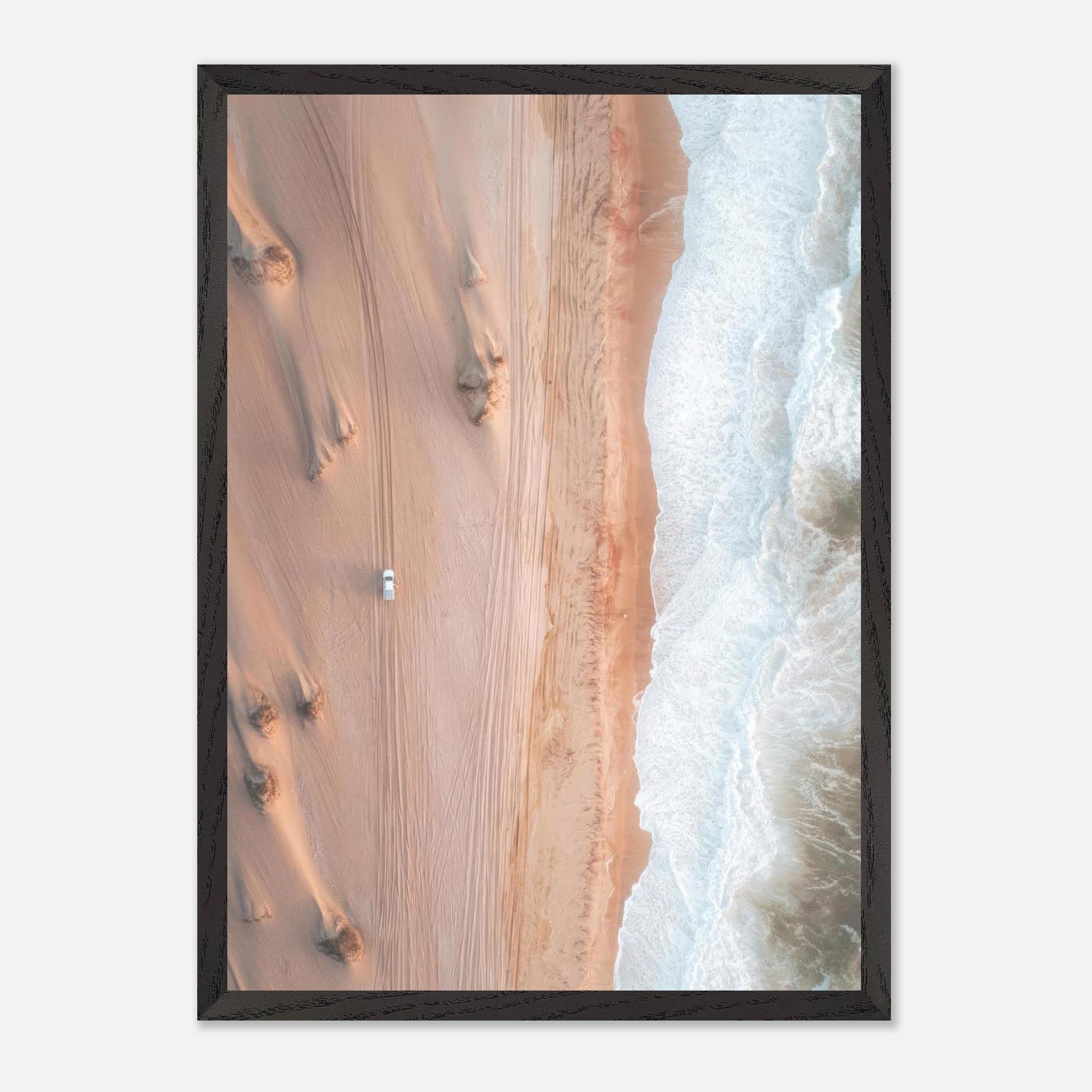 Aerial view of desert dunes meeting ocean waves in a vintage framed print, featuring a lone vehicle on sandy landscape.