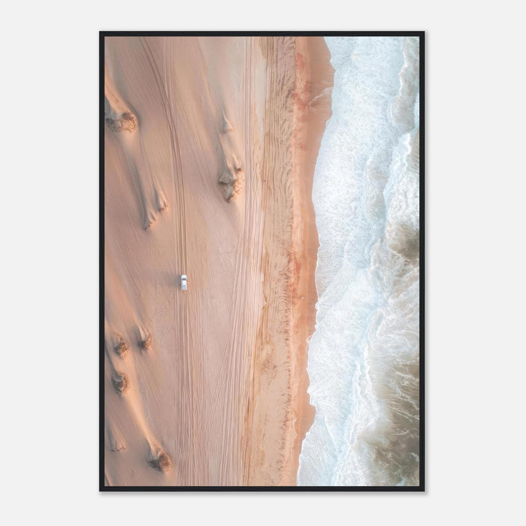 Aerial view of a vehicle on sandy dunes meeting crashing ocean waves in stunning drone photography.