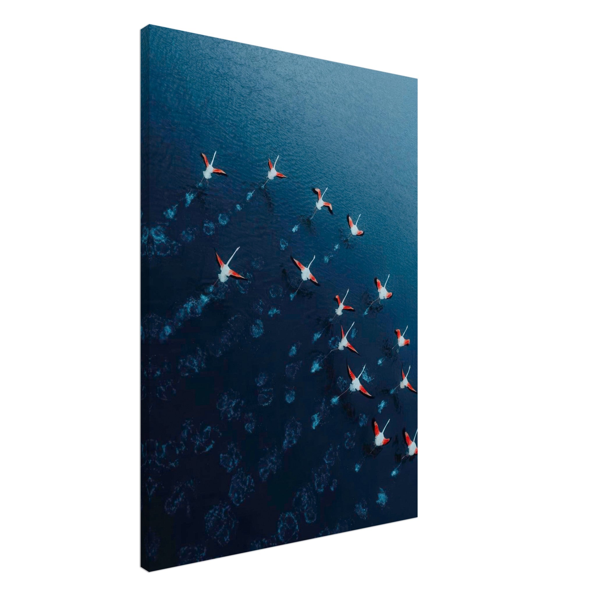 Aerial view of flamingos in flight over deep blue waters, showcasing vibrant pink and navy hues on canvas print.
