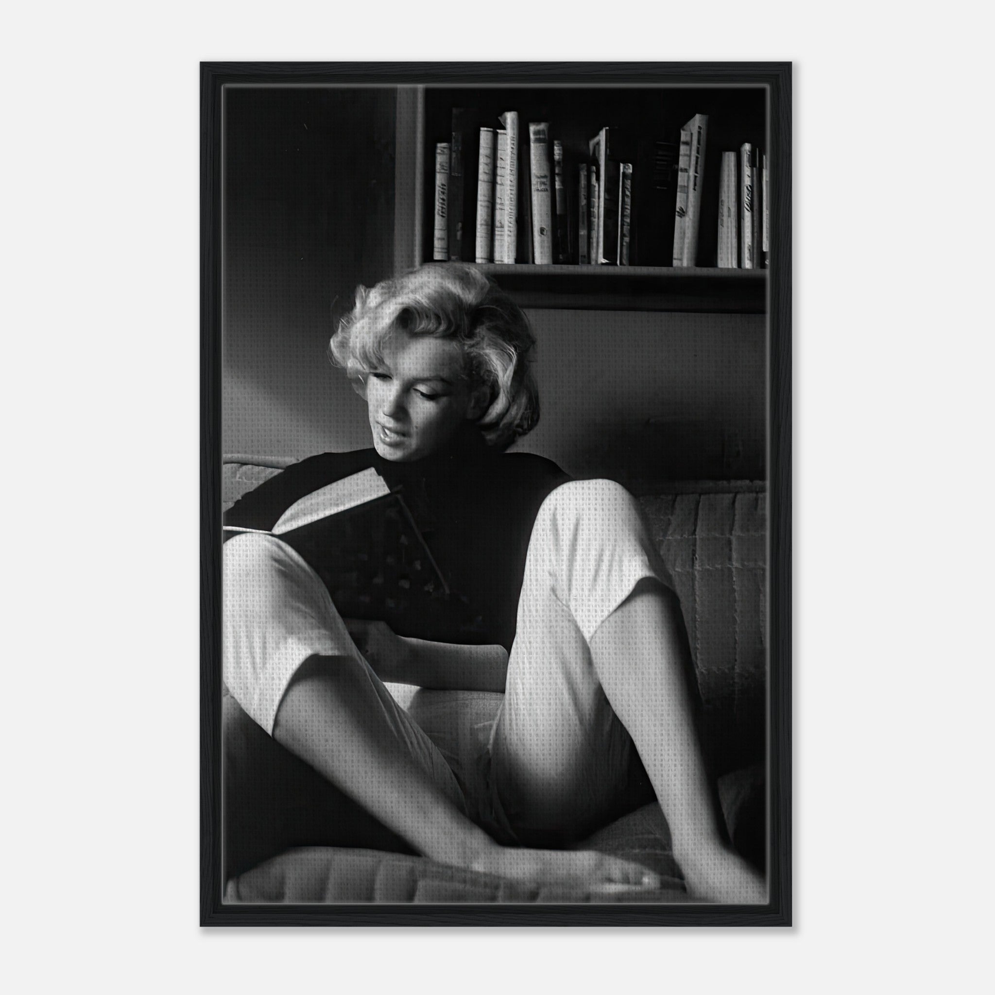 Marilyn Monroe reading a book in her home, captured in a black-and-white framed canvas artwork.