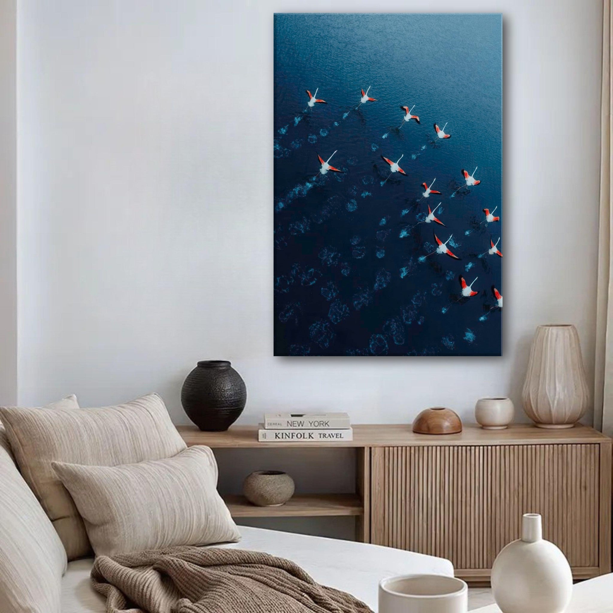 Aerial view of flamingos in flight above deep blue waters, showcased in a modern living room setting.