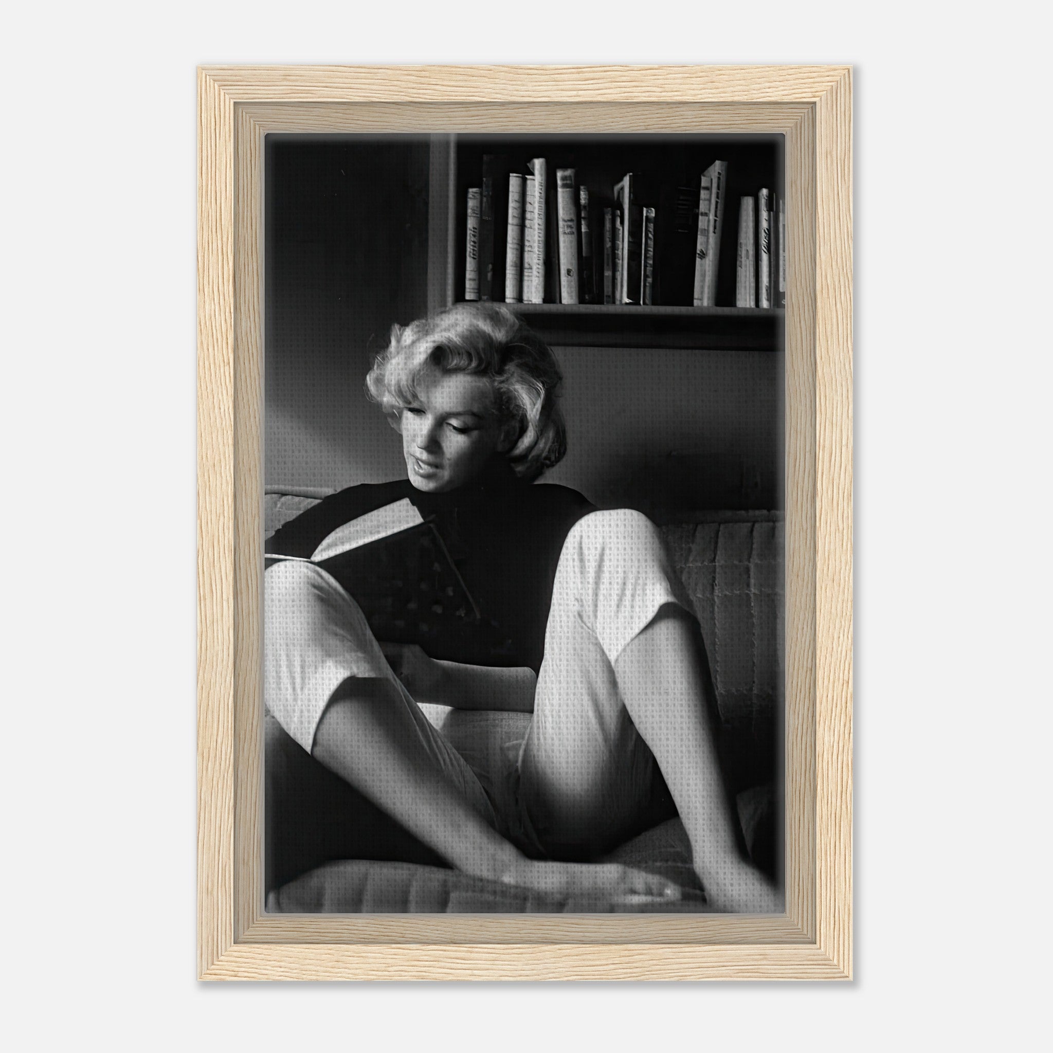 Marilyn Monroe reading at home, framed black-and-white canvas art in light wood finish.