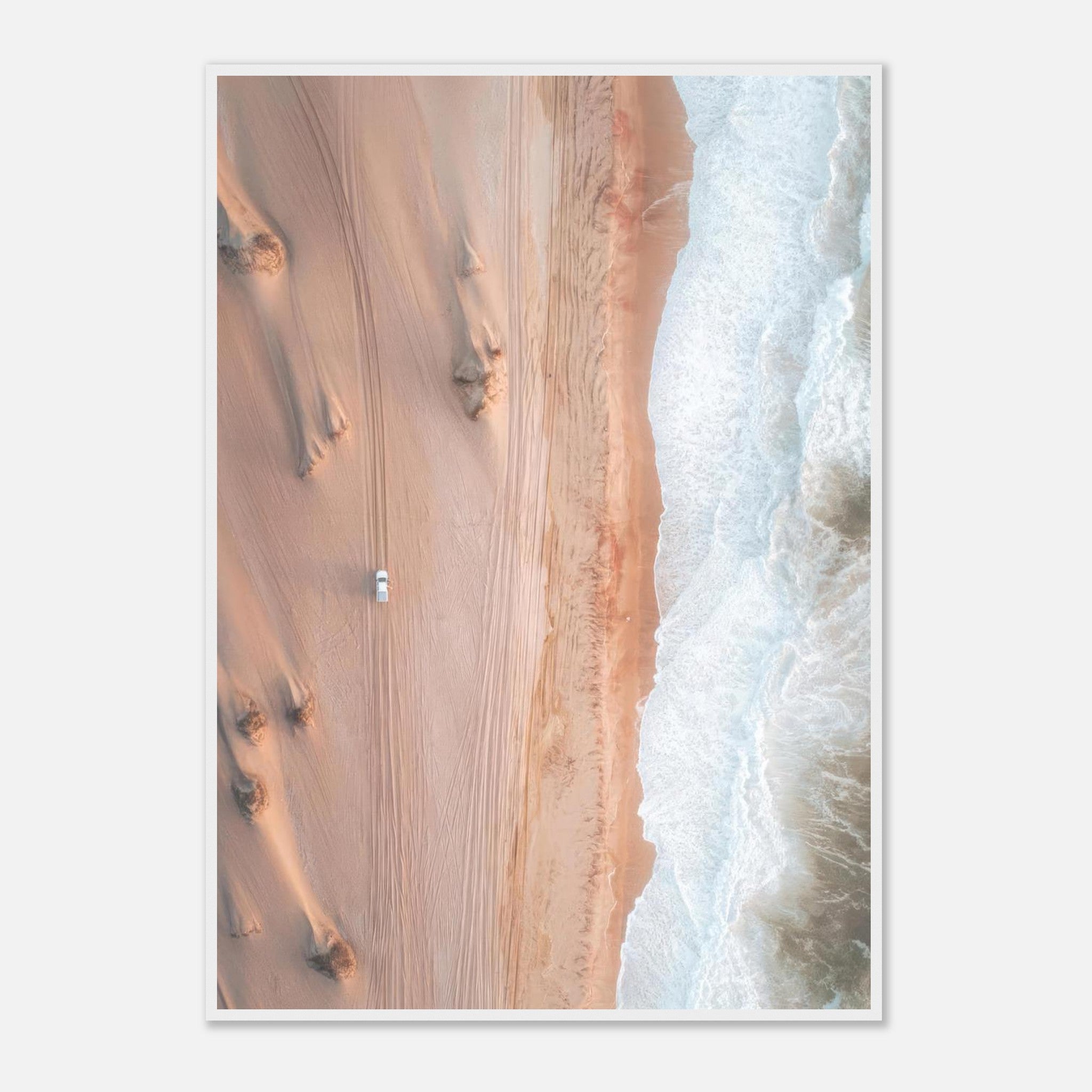 Aerial drone photography of desert sand dunes meeting ocean waves, featuring a vehicle on the sandy terrain.