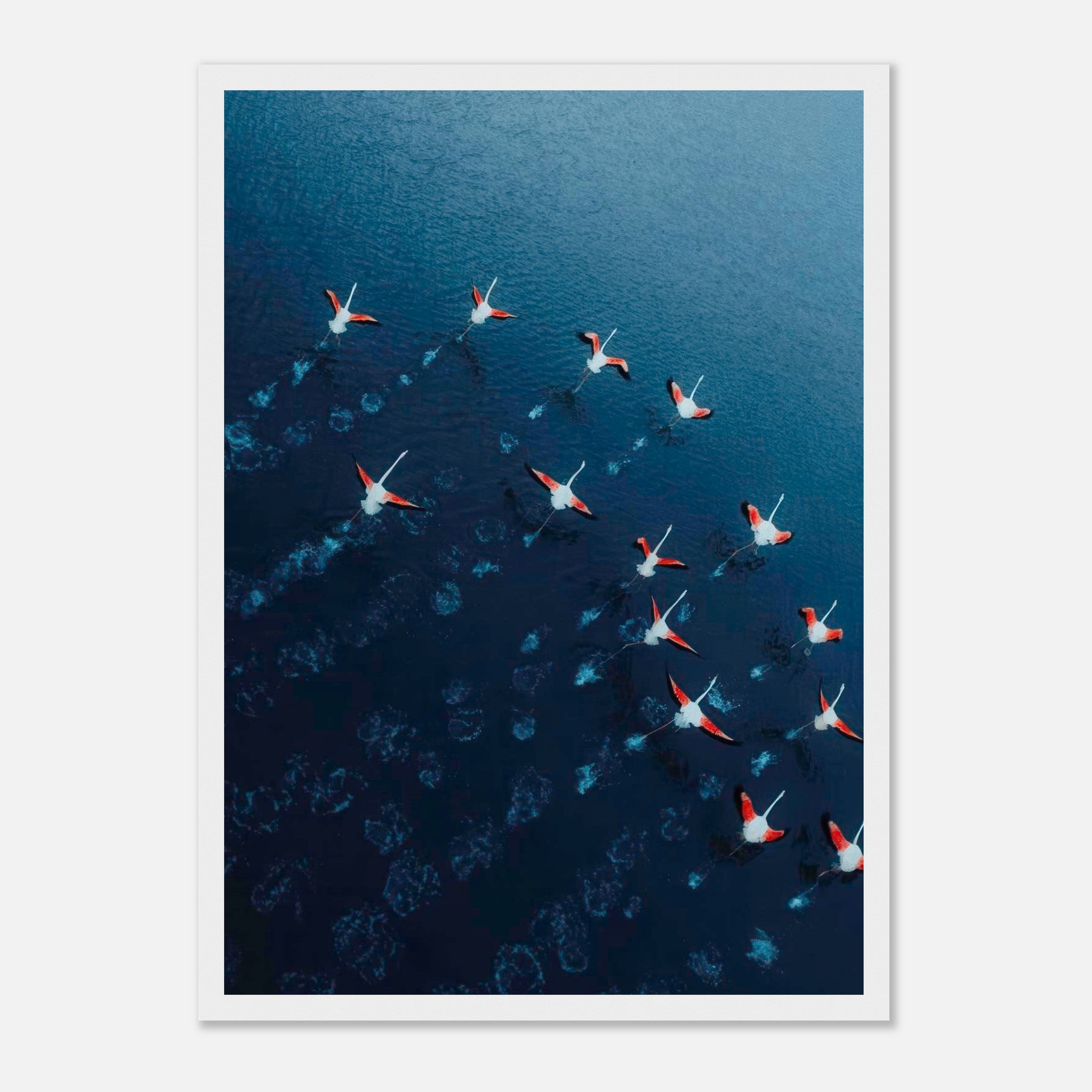 Aerial view of flamingos flying over deep blue waters, showcasing vibrant pink and navy colors in a framed print.