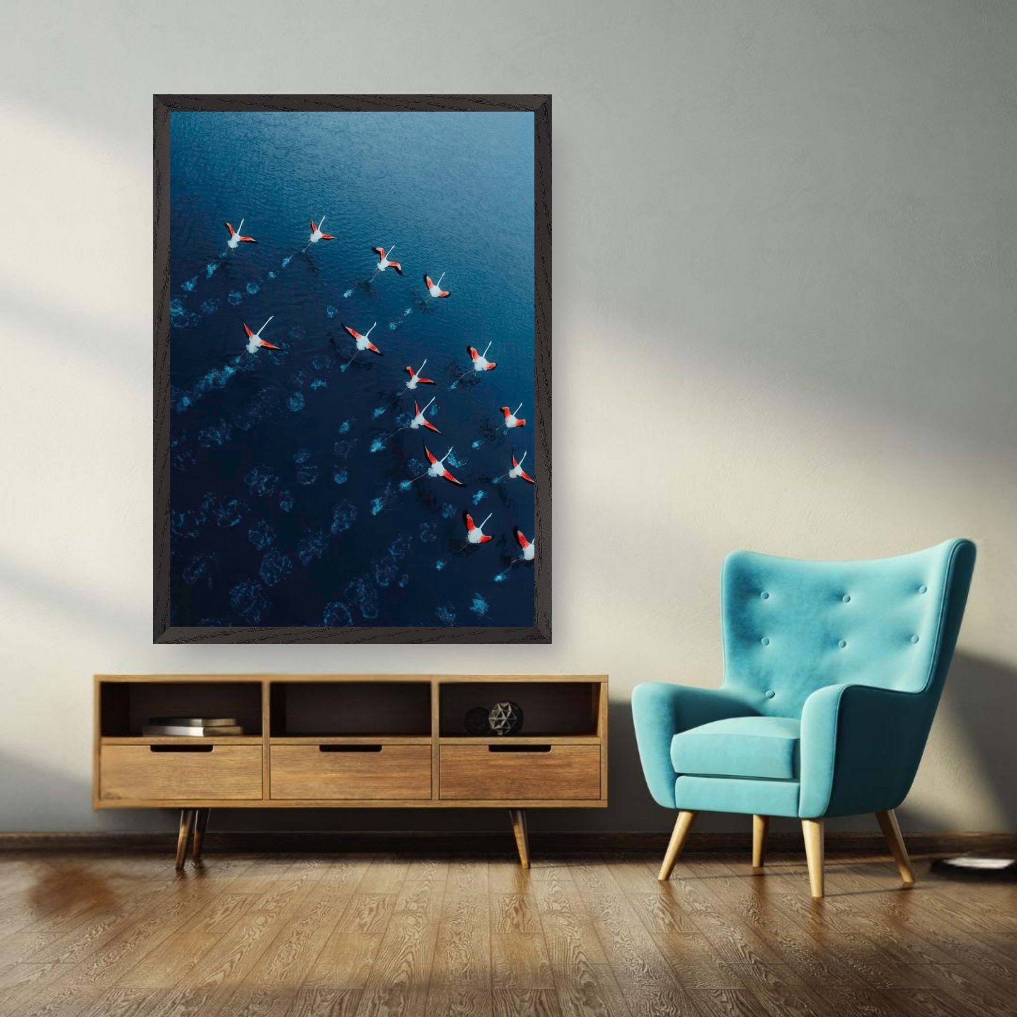 Framed aerial photograph of flamingos gliding over deep blue waters in a modern living room setting.
