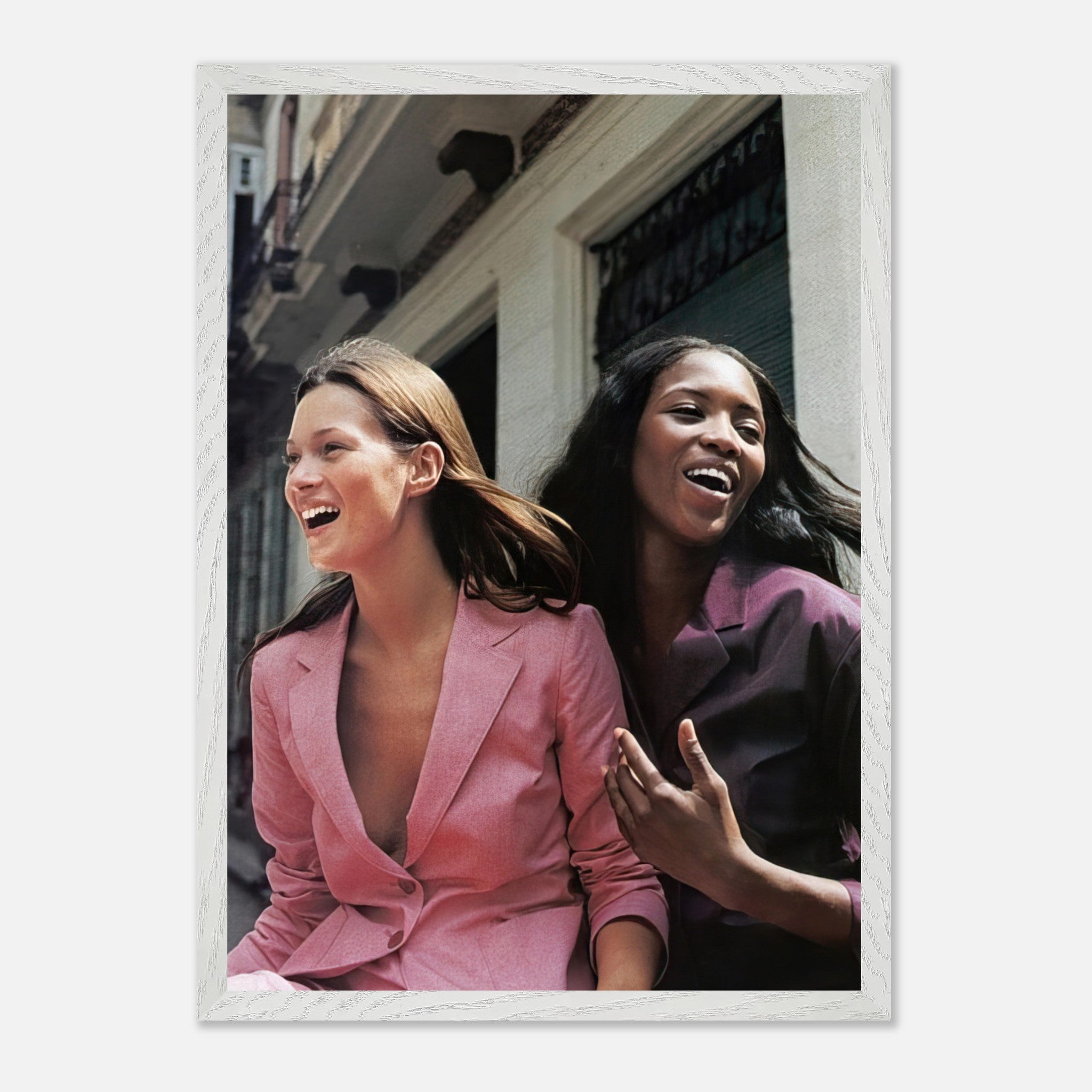 Naomi Campbell and Kate Moss candidly laughing in stylish outfits on a city street, captured in a vintage framed print.