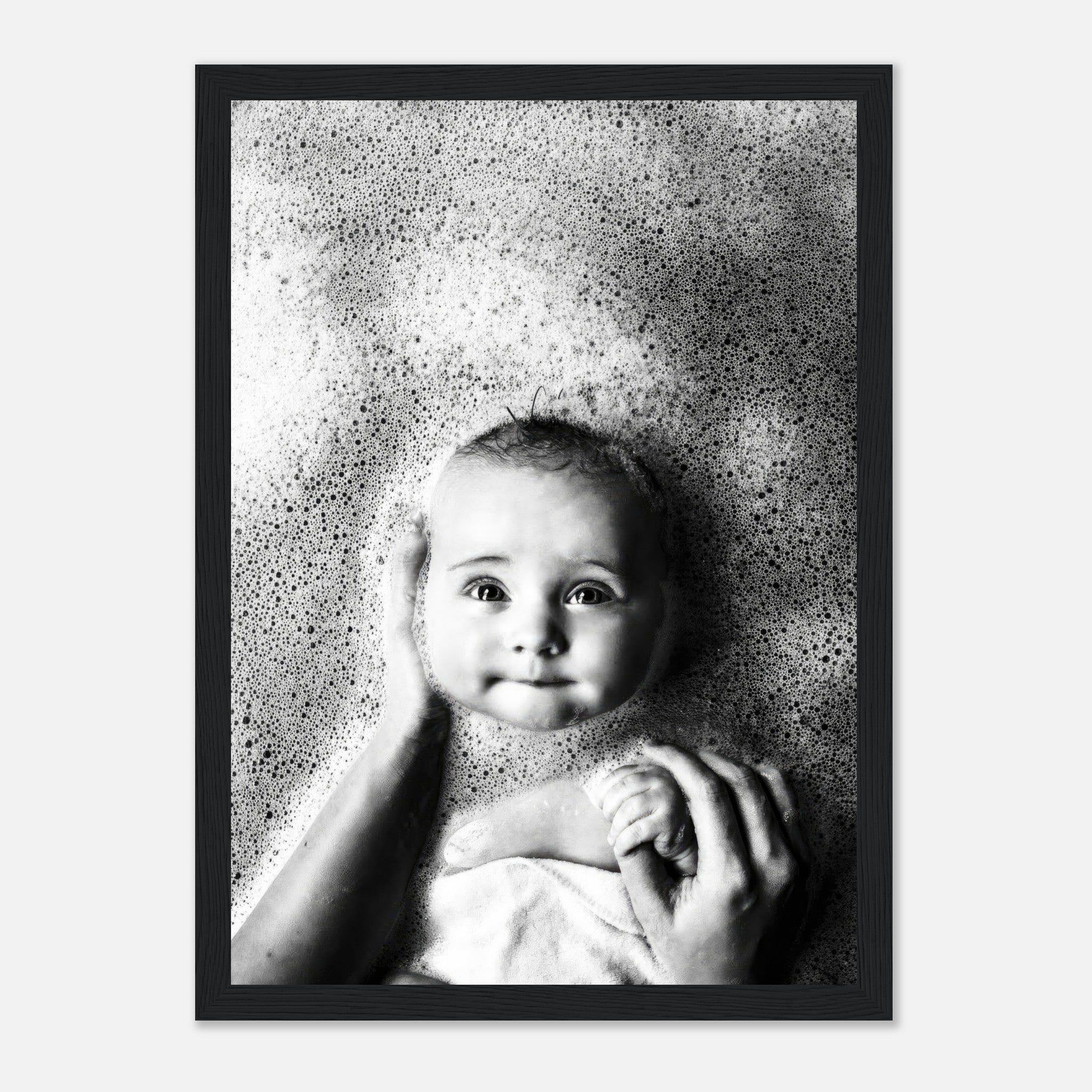 Black-and-white framed print of a baby smiling among soft bath bubbles, capturing innocence and joy.