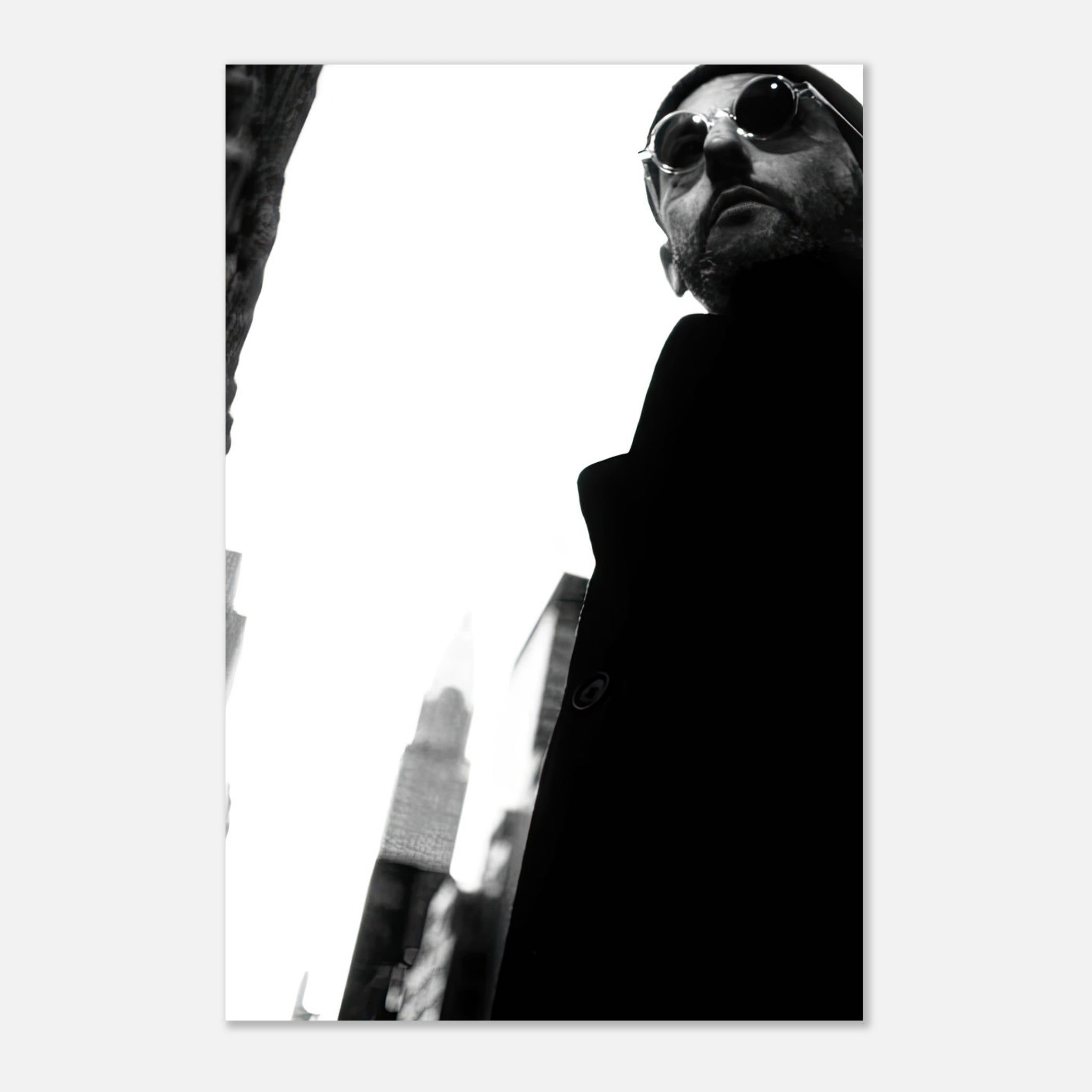 Monochrome metal print of a man in sunglasses against a dramatic urban backdrop, highlighting Jean Reno's enigmatic style.