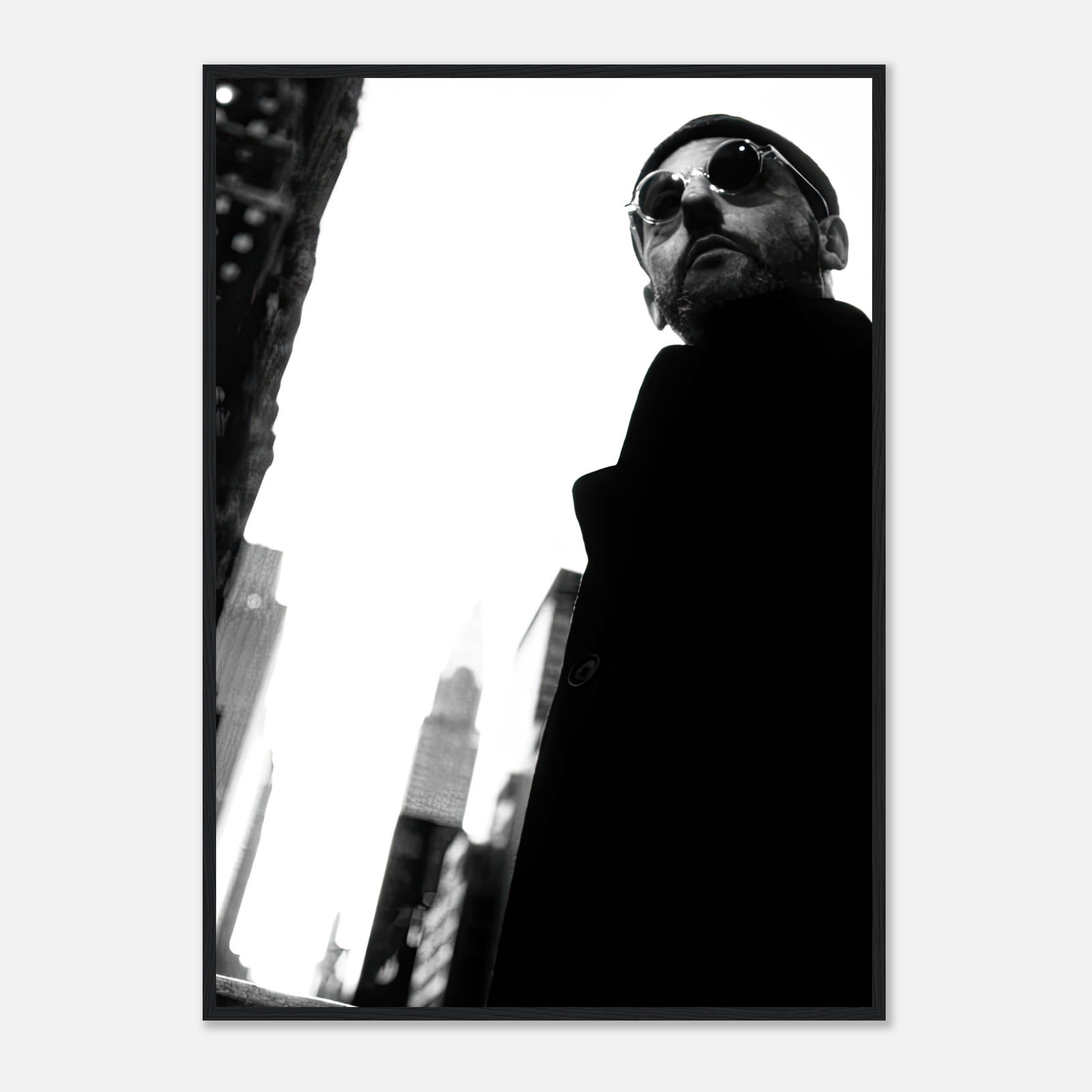Jean Reno framed print in black-and-white, showcasing cinematic artistry with urban backdrop and stylish sunglasses.