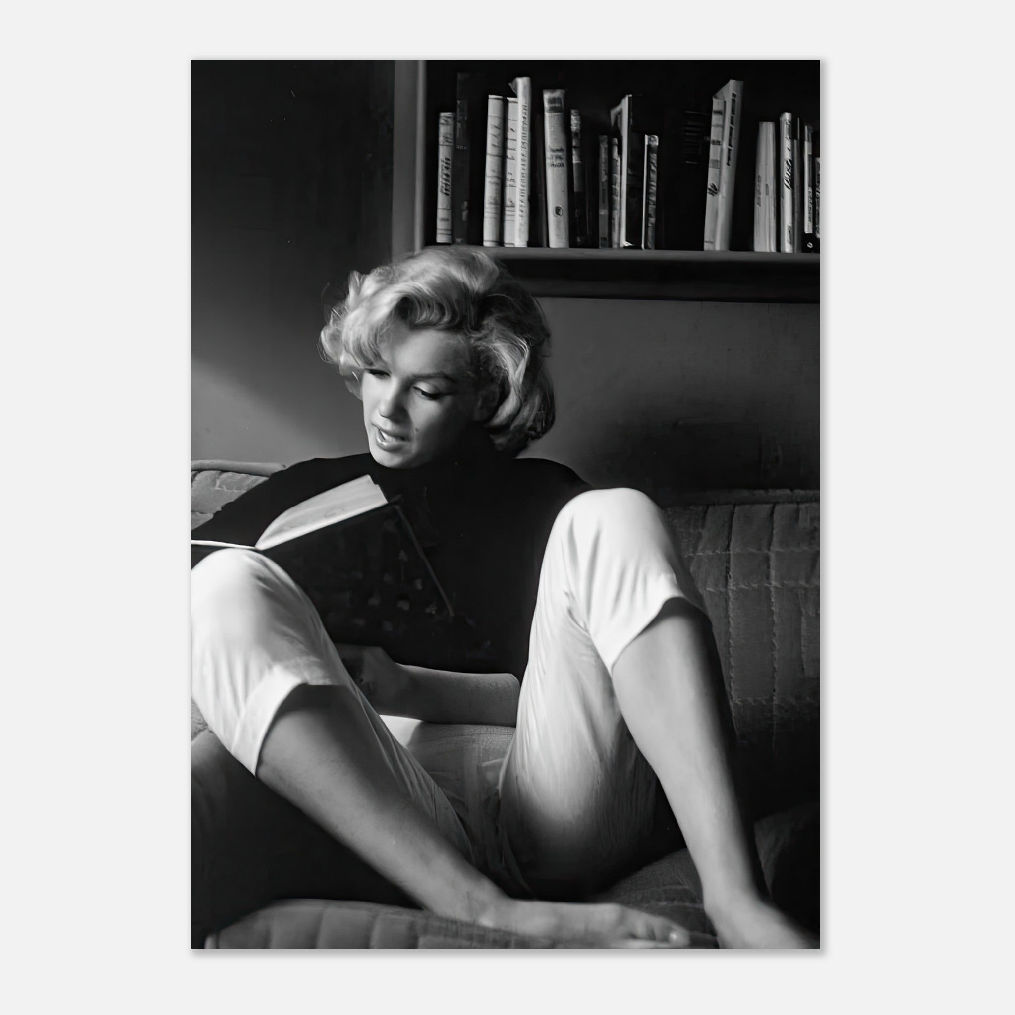 Marilyn Monroe reading a book on a sofa in a black-and-white photograph, exuding vintage elegance and charm.