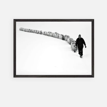 A shepherd walking through snow with his flock in a striking black-and-white fine art print.