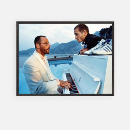 Vintage framed print of Jean Reno playing piano on the set of "The Big Blue" with a scenic seaside view.