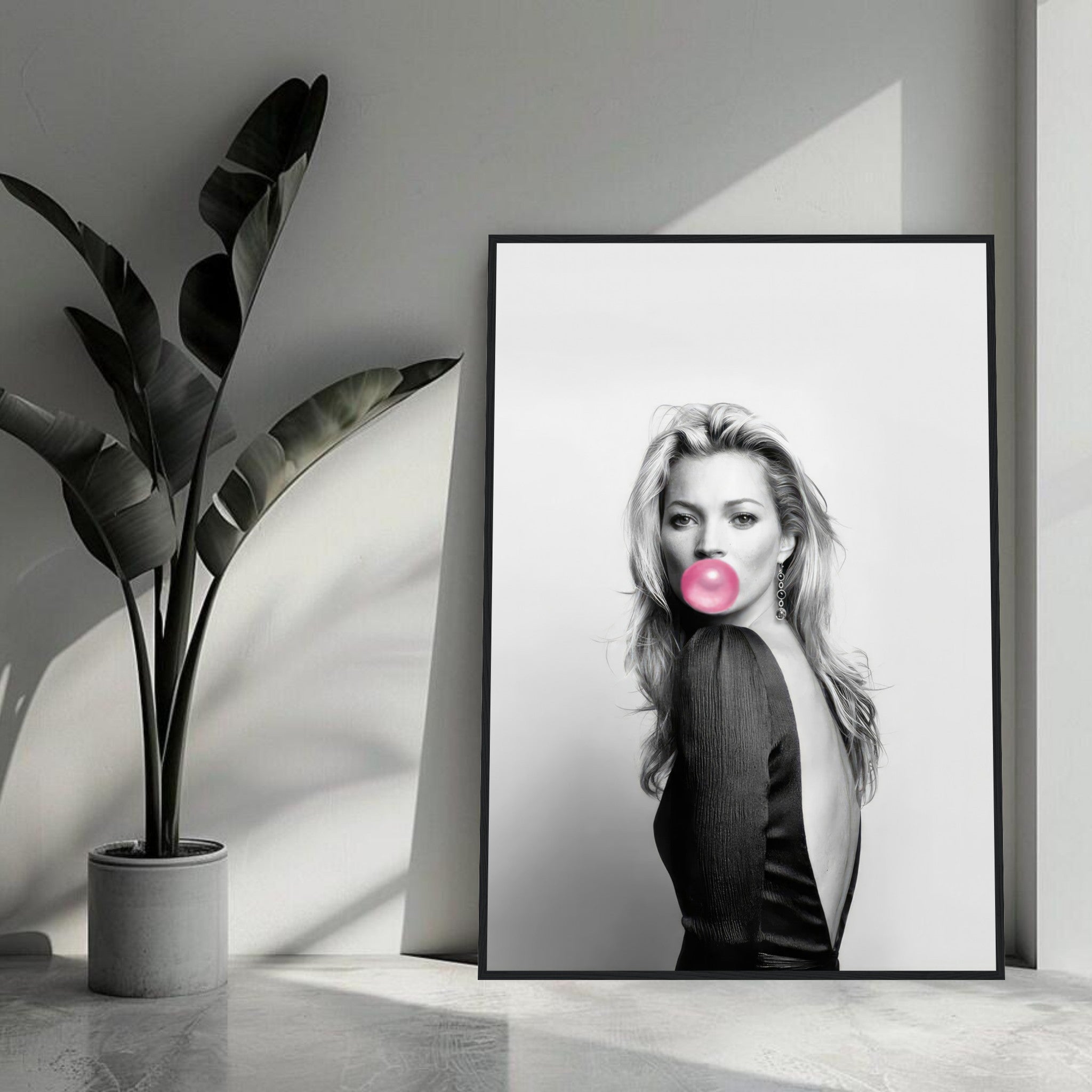 Framed print of Kate Moss blowing a pink bubble gum in a chic modern setting with plants.