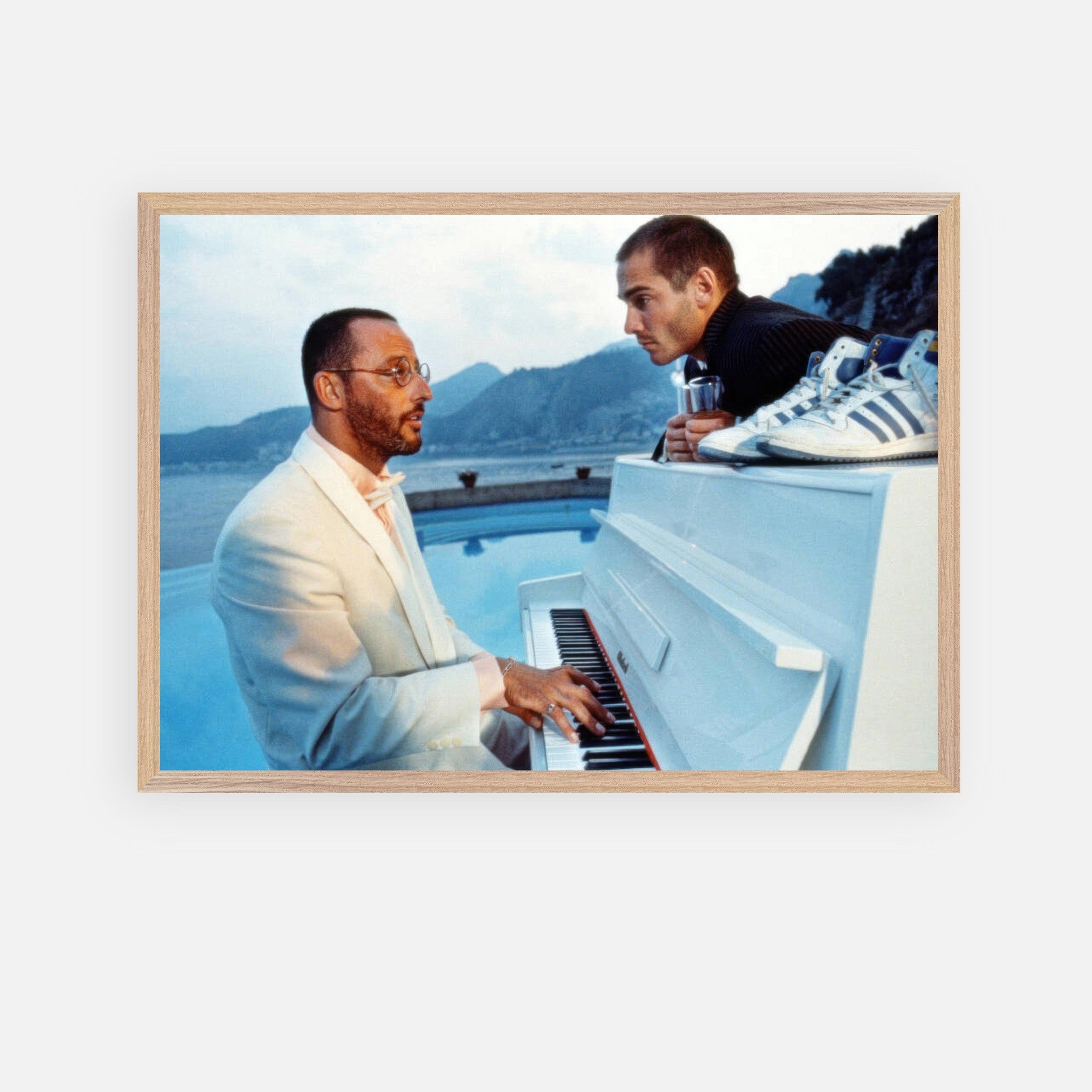 Jean Reno playing piano on set of "The Big Blue," framed print with serene seaside backdrop and classic cinematic vibe.