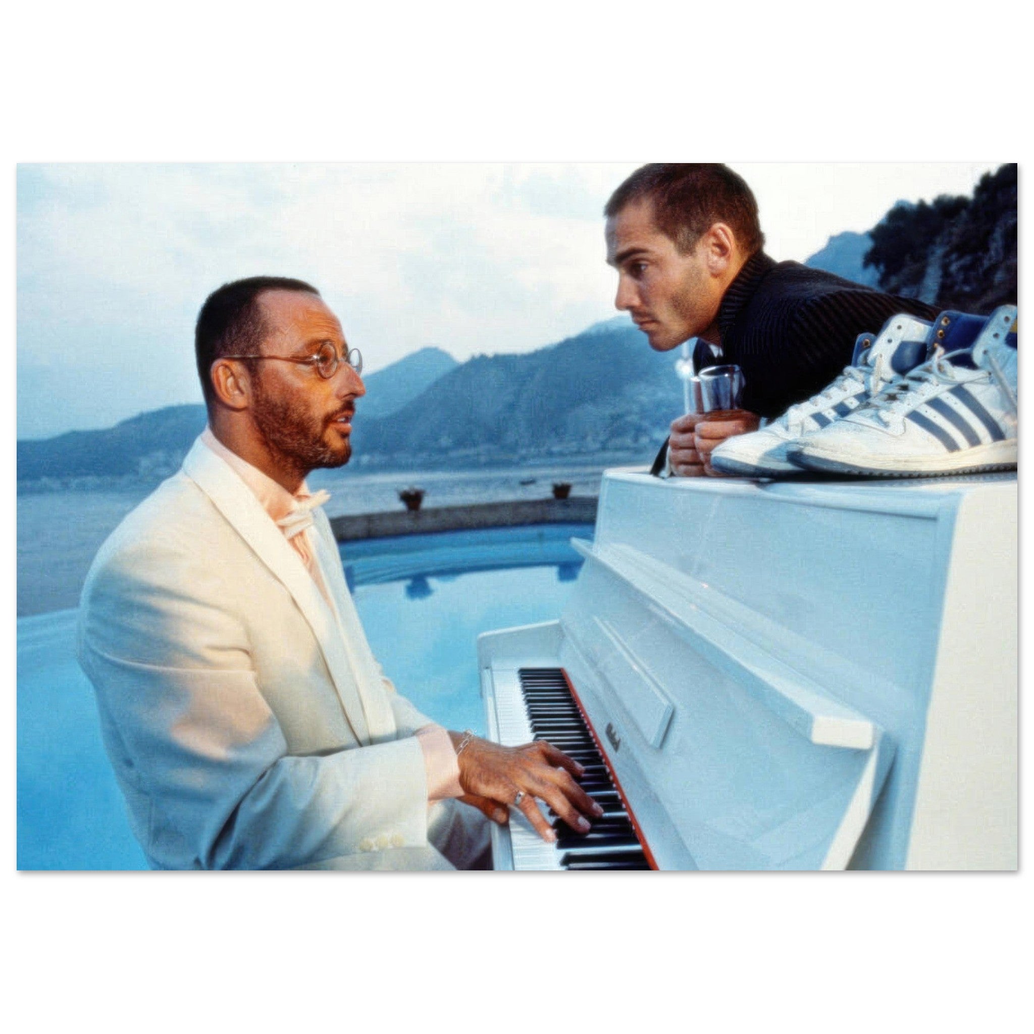 Jean Reno playing a white piano with a coastal backdrop, capturing an iconic moment in high-quality photography.