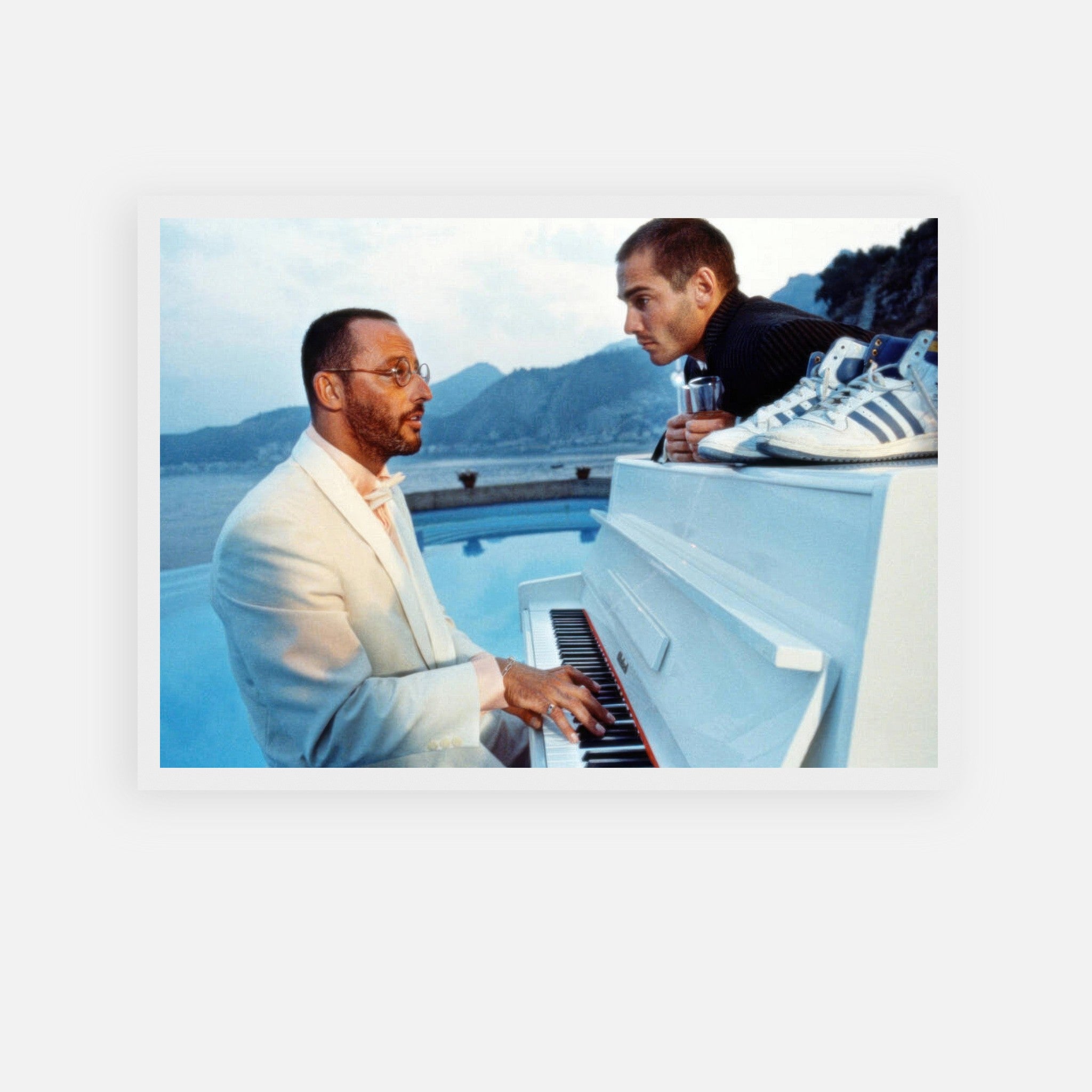 Jean Reno playing piano in "The Big Blue" film scene with serene ocean backdrop and mountains, framed print artwork.