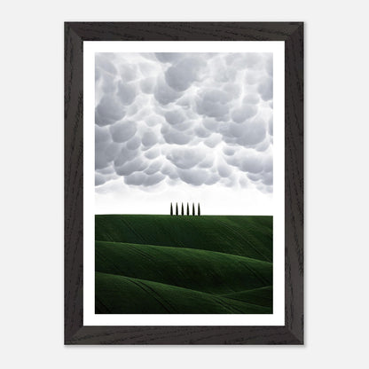 Vintage framed art depicting rolling green hills and cypress trees under a dramatic sky in Tuscany, Italy.