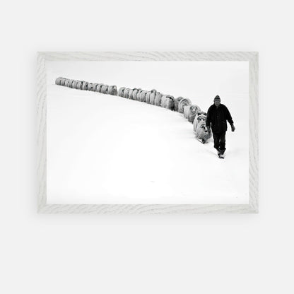 Black-and-white photo of a shepherd guiding sheep through a snow-covered landscape, framed in vintage style.