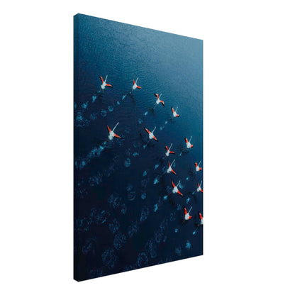 Aerial view of flamingos flying over deep blue waters in vibrant pink and navy hues on a canvas print.