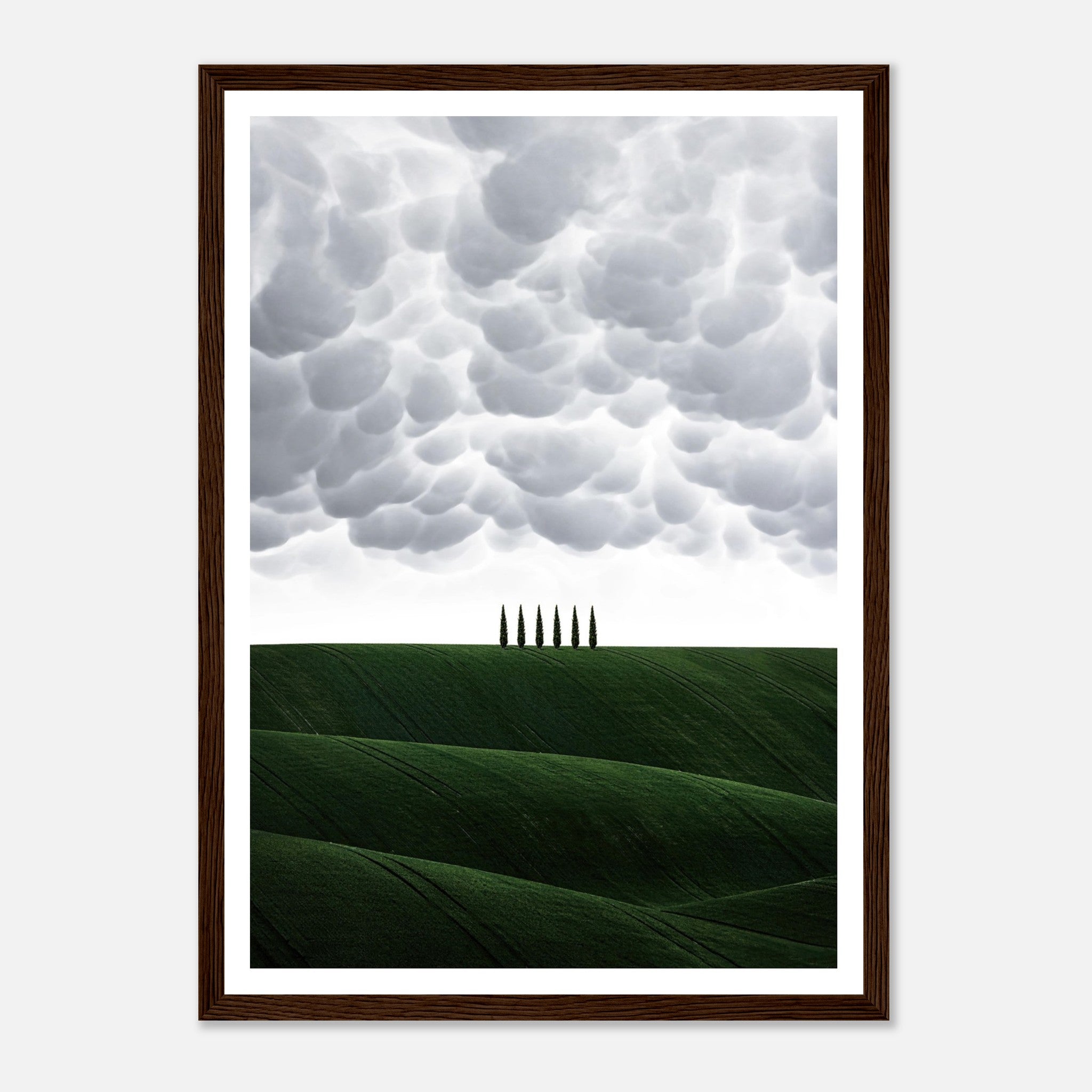 Framed print of rolling green hills under dramatic clouds with cypress trees in Tuscany, Italy.