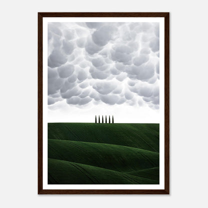 Framed print of rolling green hills under dramatic clouds with cypress trees in Tuscany, Italy.