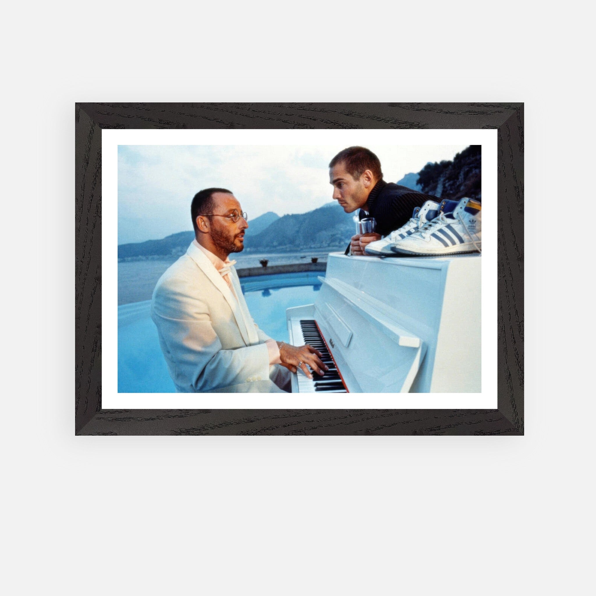 Jean Reno playing piano in a vintage framed print from "The Big Blue," featuring a scenic seaside backdrop.