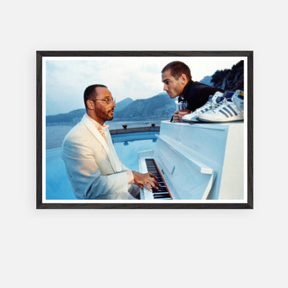 Vintage framed print of Jean Reno at the piano on set of "The Big Blue," featuring a serene seaside backdrop.