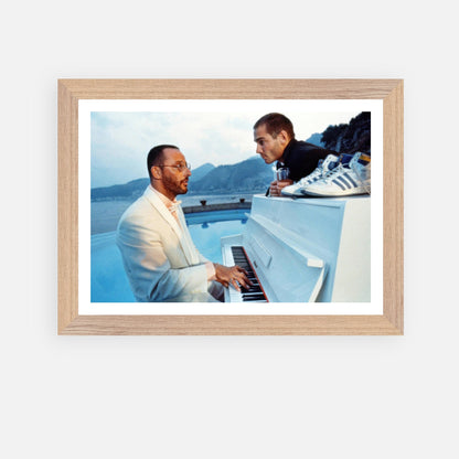 Vintage framed print of Jean Reno playing piano on the set of "The Big Blue" by the seaside. Classic cinema art.