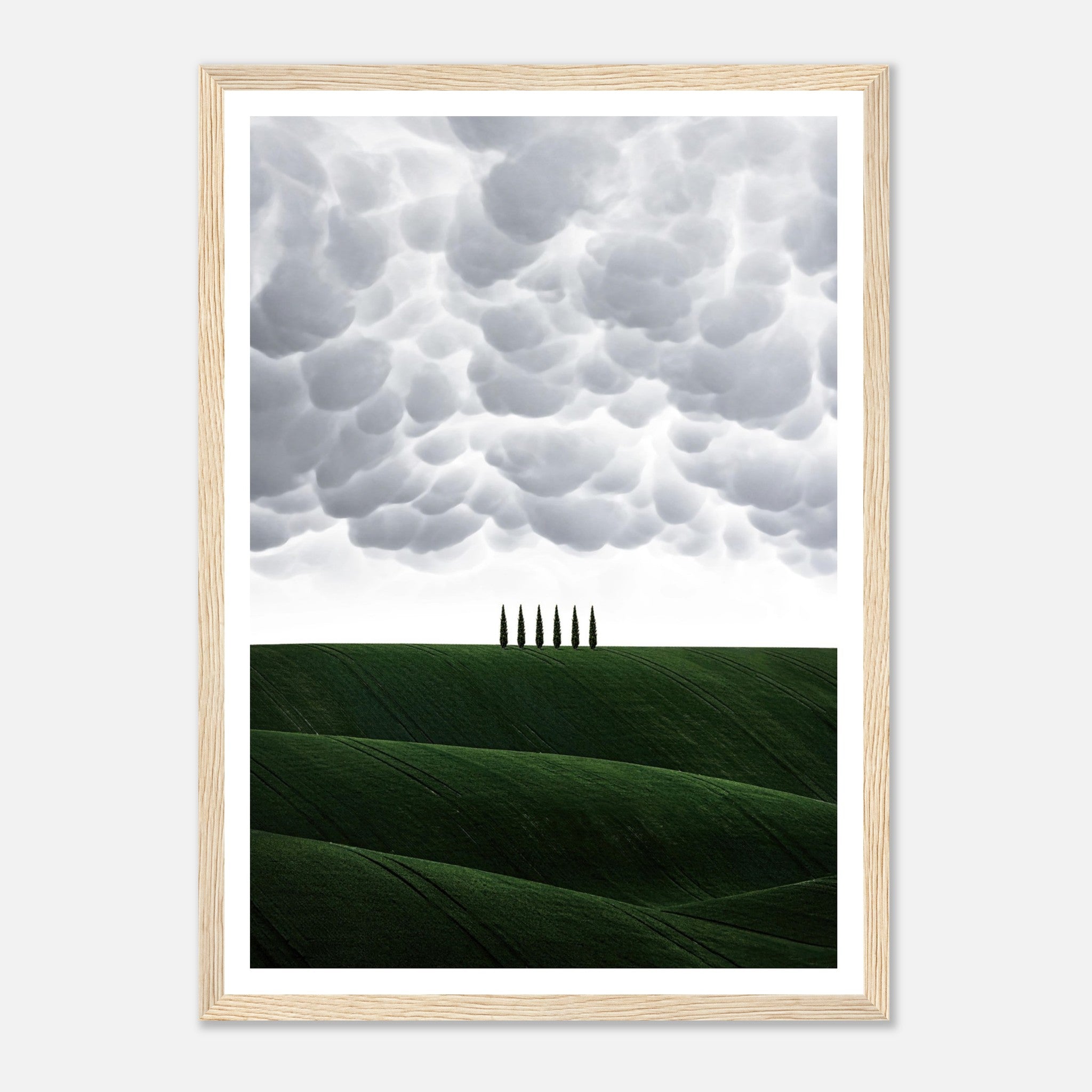 Framed print of rolling green hills and cypress trees under dramatic clouds, capturing the beauty of Tuscany, Italy.