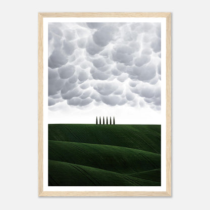 Framed print of rolling green hills and cypress trees under dramatic clouds, capturing the beauty of Tuscany, Italy.