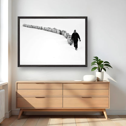 A shepherd leading his flock through snow in a black-and-white fine art print, framed on a modern wall.