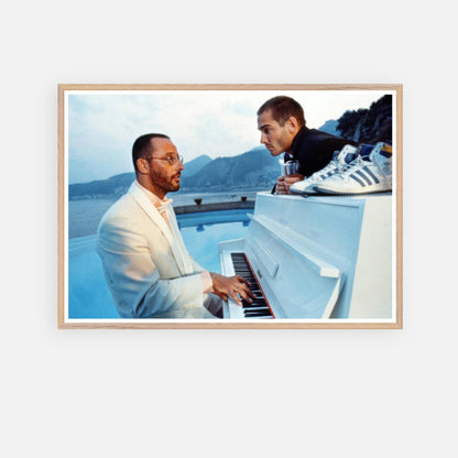 Jean Reno playing piano on set of "The Big Blue," vintage framed print with serene seaside backdrop.