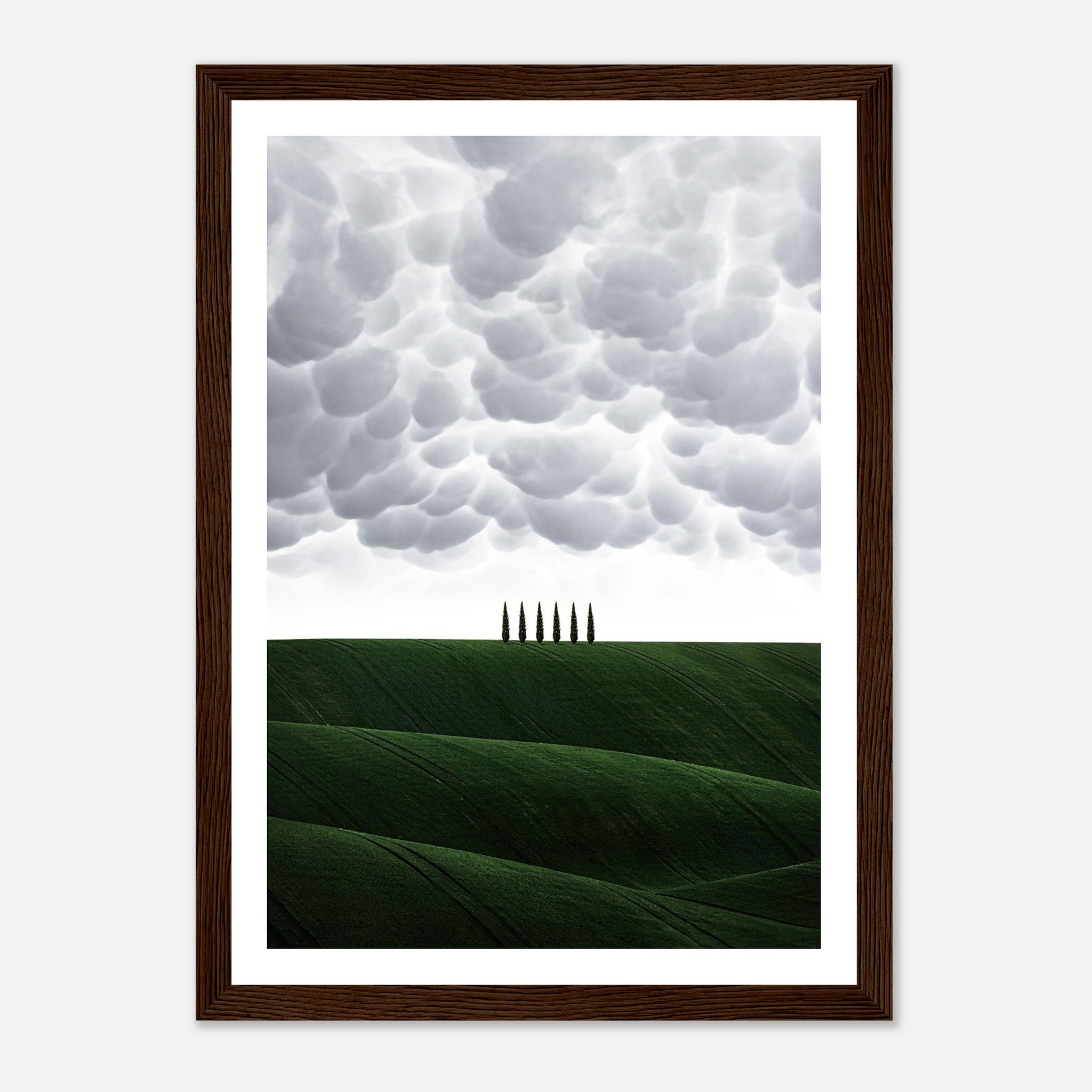 Framed print of Tuscany with rolling green hills and cypress trees under dramatic cloud formations.